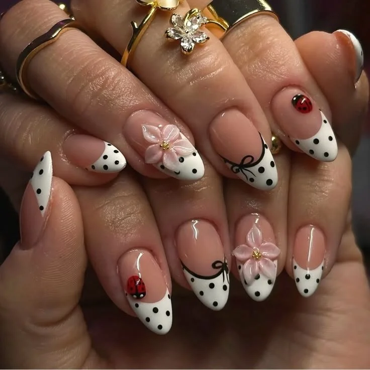 Polka dot nails with French tips, pink flowers, and ladybug accent design.
