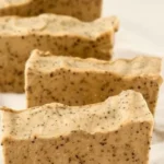 A bar of cold process coffee soap with coffee beans on a wooden surface.