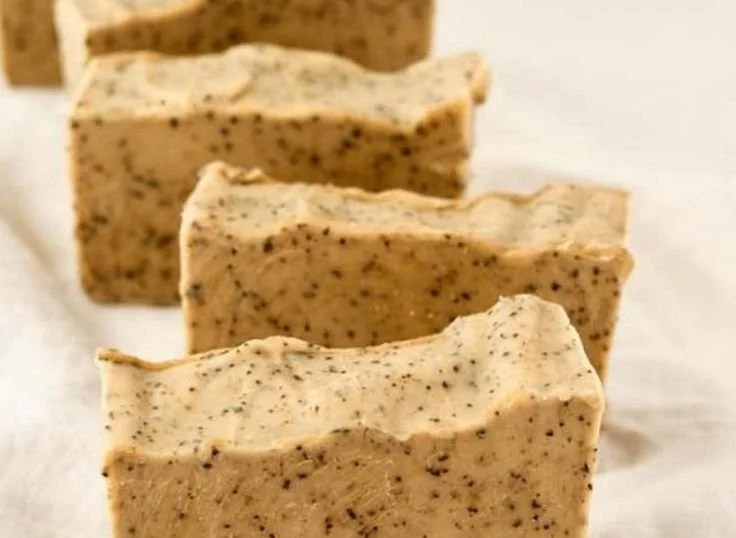 A bar of cold process coffee soap with coffee beans on a wooden surface.
