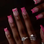 Hot pink nails featuring bow charms and French tip designs for a chic manicure.