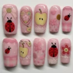 Cute pink ladybug press on nails with apple and flower designs in pastel colors.