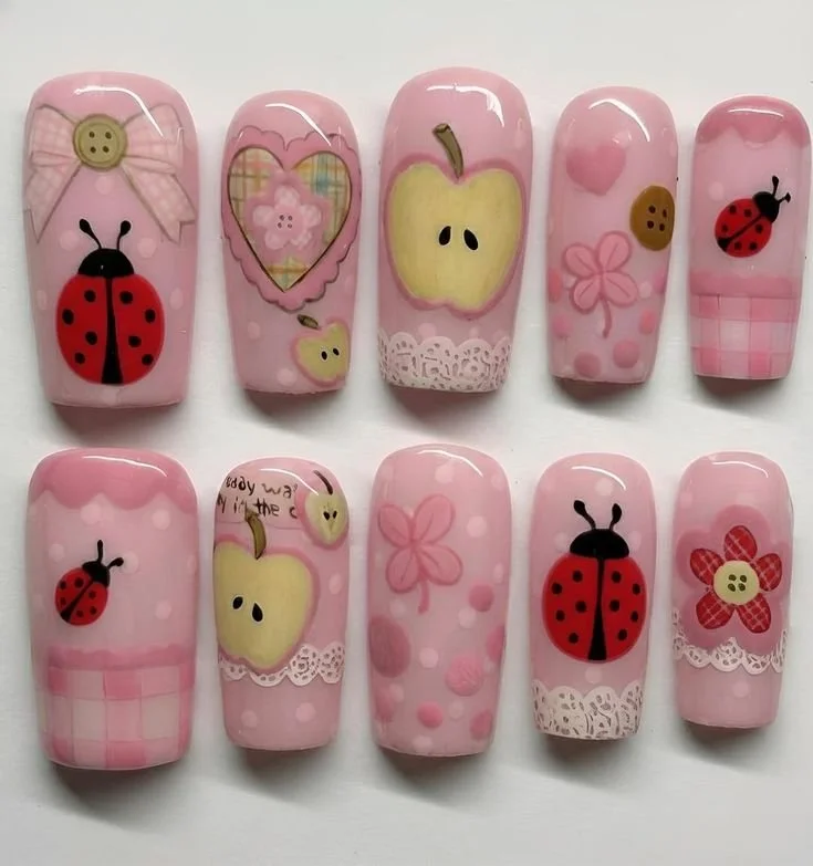 Cute pink ladybug press on nails with apple and flower designs in pastel colors.