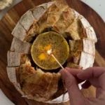Homemade butter candle beside fresh sourdough bread on a wooden table.