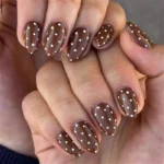 White polka dot brown nail art for fall and winter on short almond fake nails.